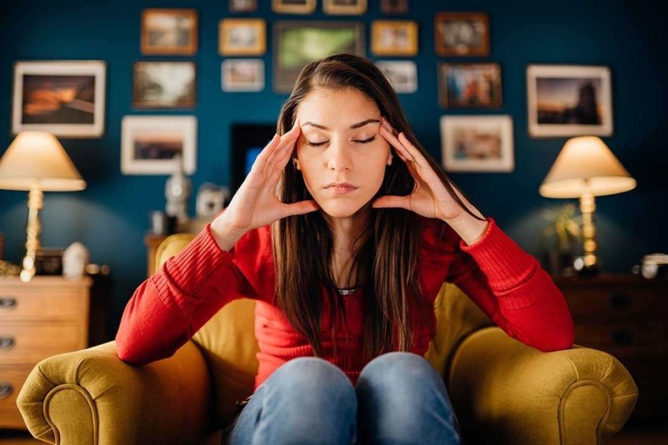 Overthinking young woman holding head sitting in chair