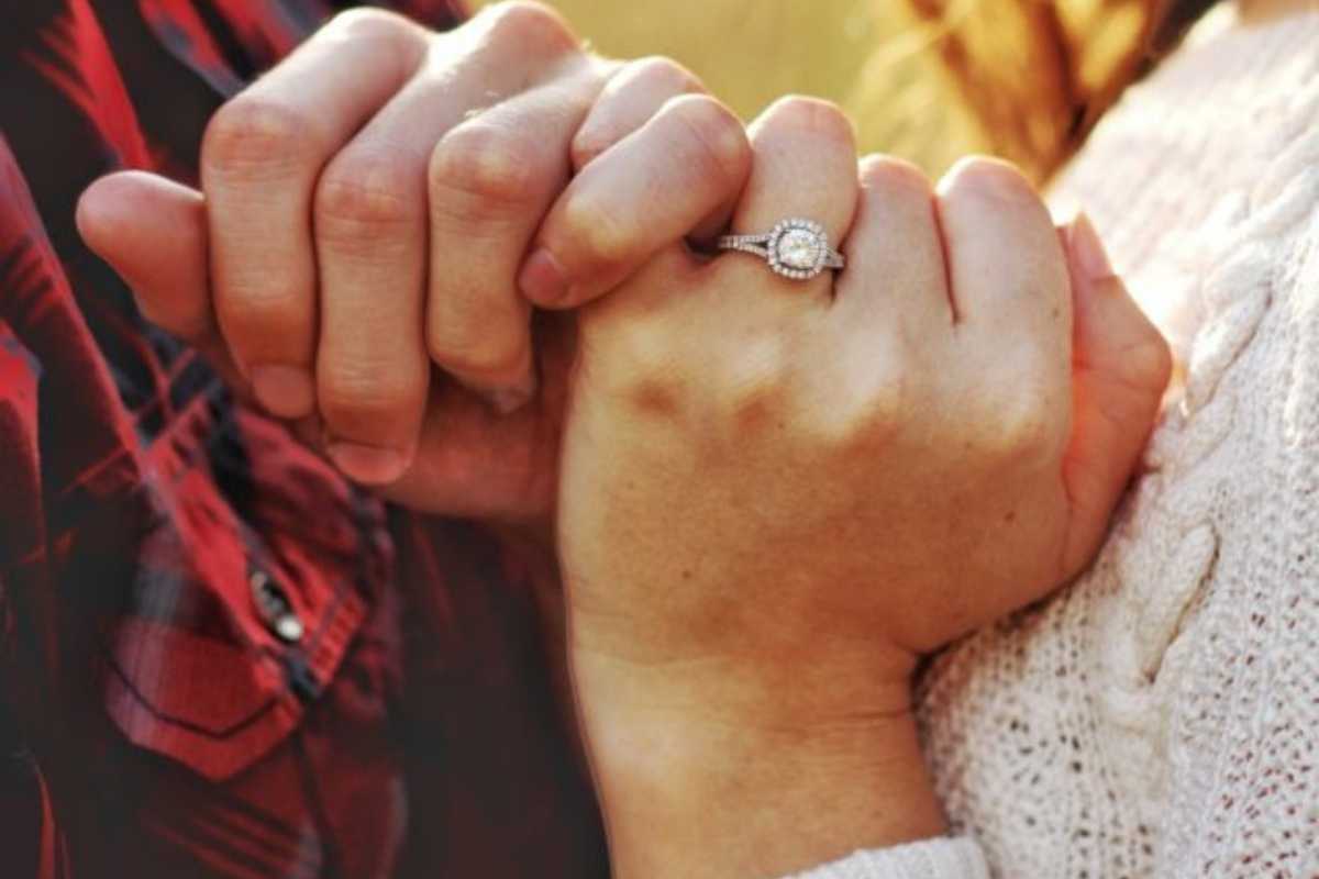 Two hands holding each other with an engagement ring as the sun glows behind them beginning premarital counseling services