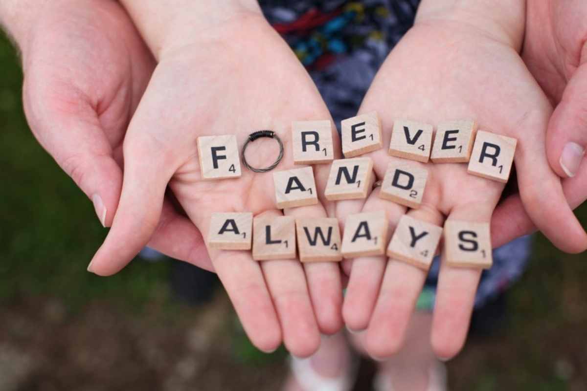 Two engaged couple hands supporting each other with the phrase "Forever and Always" in Scrabble tiles on the hands pre-marital